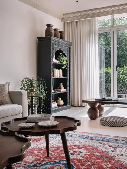 The living area is a treasure trove of collected items, with a traditional carved bookshelf, antique pottery, and a mix of seating that overlooks the garden.