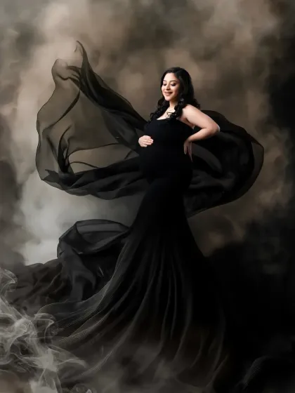 The power and elegance of a mother-to-be. This dramatic portrait features a black gown with a sheer, flowing train that blends into a smoky, atmospheric background. We use this technique to create a sense of mystery and fine-art beauty.