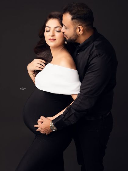 A classic pose full of love and affection. The partner's embrace from behind is a beautiful way to showcase their connection and the baby bump.