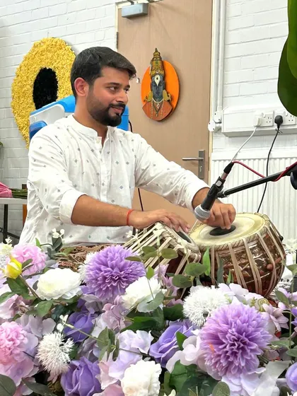 Playing at the devotional concert in the UK, surrounded by flowers and the serene presence of the deities.