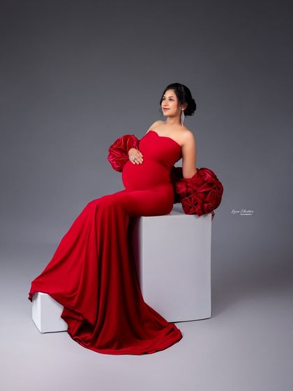 A seated pose in a striking red gown, showing off the unique rose-like sleeves. This look is both elegant and fashion-forward.