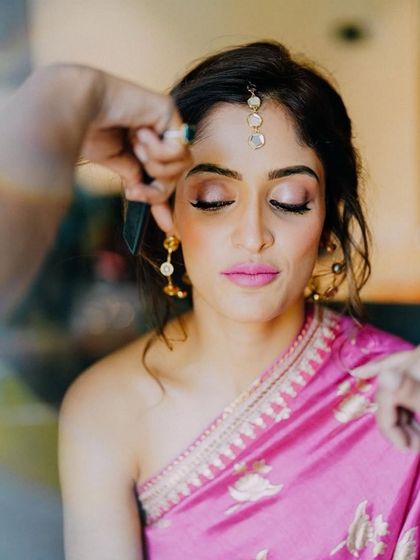 A behind-the-scenes moment of creating Deepali's Haldi look. The focus is on a soft, pink-toned eye makeup that complements the bold fuchsia lip, creating a harmonious and vibrant look.