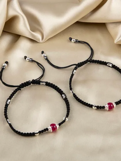 A pair of black cord anklets with a central red bead.