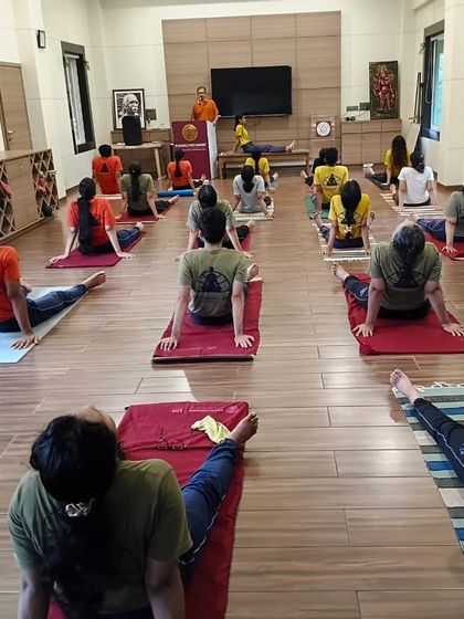 A class of students practices a foundational backbend asana. The uniform practice demonstrates a disciplined environment where everyone moves together, guided by the instructor's voice and demonstration.