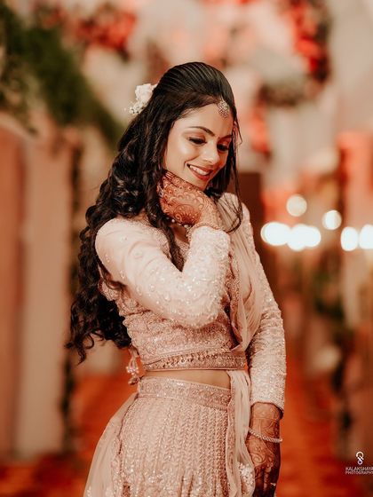 A beautiful candid portrait of a bride in a soft pink lehenga, smiling gently.