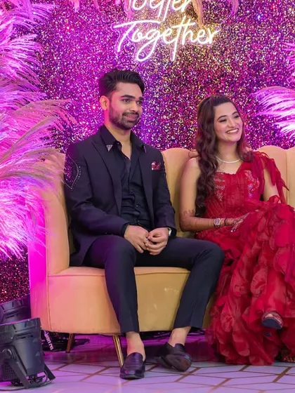 The couple seated on a plush sofa against a glittering pink backdrop, their smiles lighting up the room. The decor is designed to make them the center of attention.