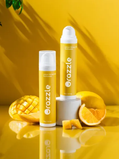 A hero shot of lemon and mango flavored toothpaste. We used a sunny yellow background with a reflective surface and fresh fruits to create a bright, energetic composition, with leafy shadows adding a touch of nature.