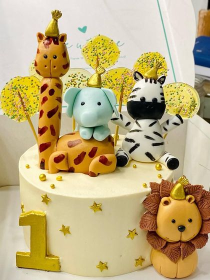 A party in the jungle for a first birthday! This cake features adorable, hand-molded fondant animals including a giraffe, elephant, zebra, and lion, all wearing tiny party hats.