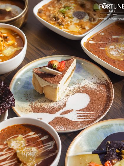 A table showcasing both savory and sweet. Our Tiramisu, with its delicate cocoa powder art, stands alongside rich Indian curries, representing the diverse menu at Zodiac.