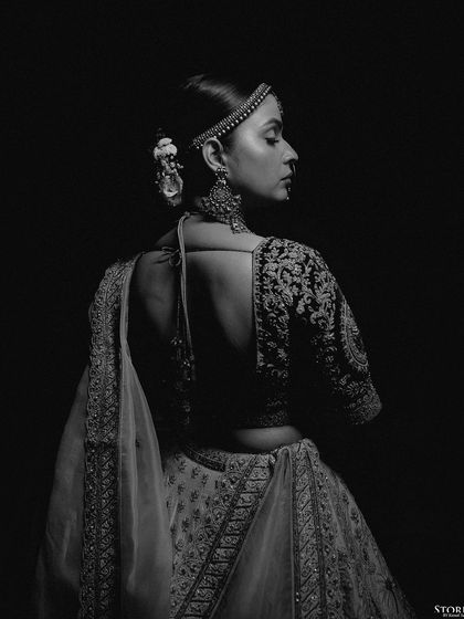 A dramatic black and white portrait of the bride from behind, highlighting the intricate details of her blouse and hairstyle.