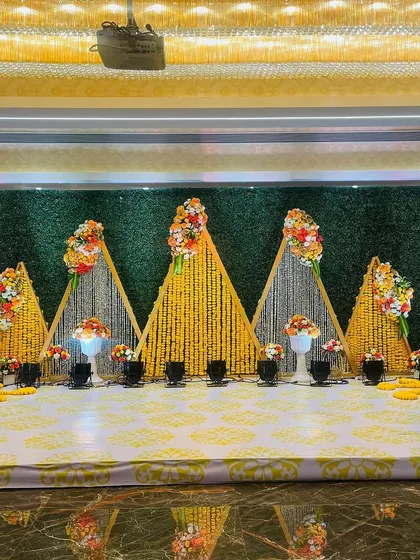 This Haldi stage features a unique geometric design. I used triangular frames decorated with marigold garlands against a green hedge wall to create a modern and visually interesting backdrop.
