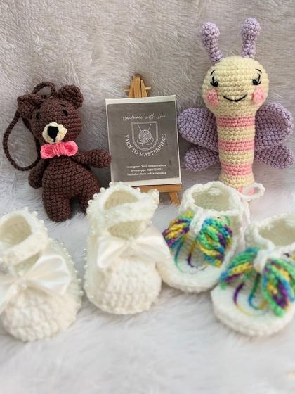 An assortment of baby items I've made, including different styles of booties, a butterfly rattle, and a small bear keychain.
