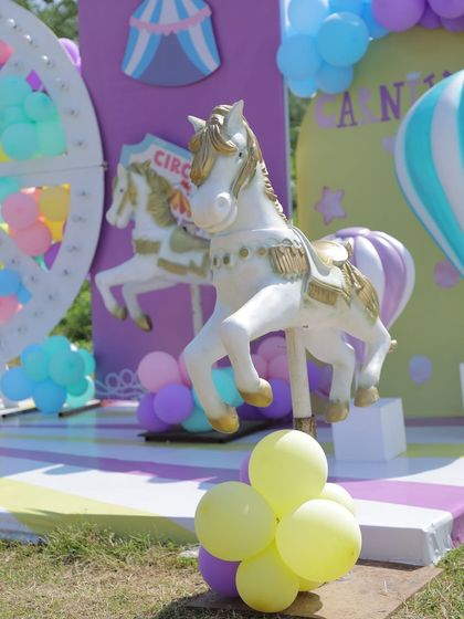 A detailed shot of a carousel horse prop at an outdoor carnival party. The combination of pastel balloons and the classic white horse creates a timeless and magical photo spot.