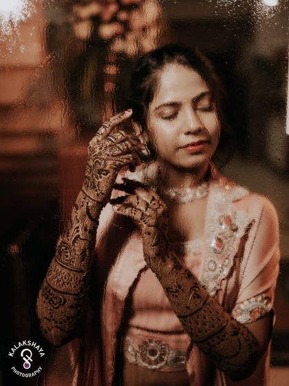 An artistic shot of the bride showing off her intricate Mehendi design through a rain-streaked window.