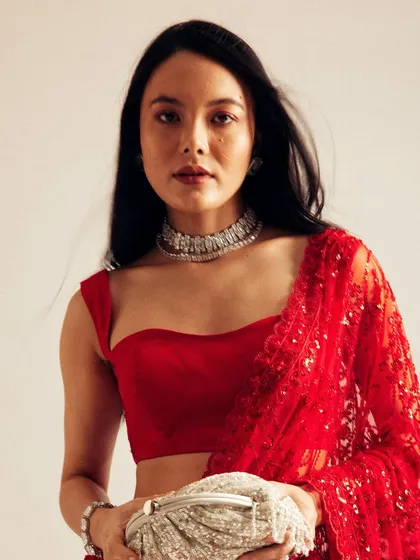 A softer, more direct-to-camera shot from the same series. The clean makeup and natural hair movement highlight the model's features and the elegance of the red saree.