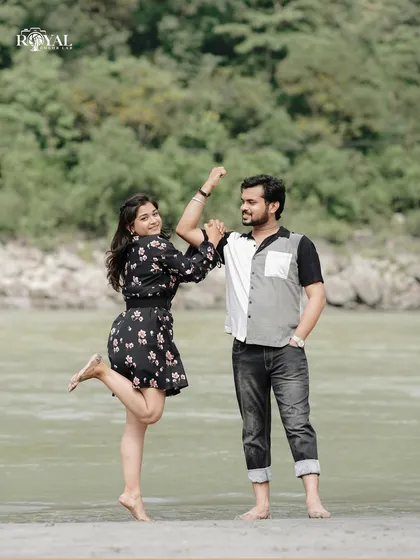 A fun and playful shot of a couple by the river, with the woman striking a joyful pose.
