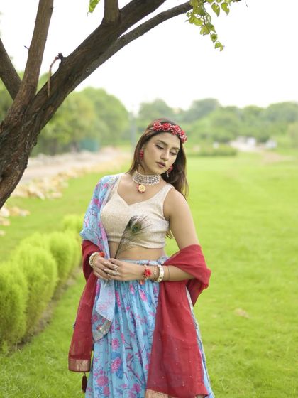 A serene Janmashtami look. I’m wearing a beautiful blue and red lehenga with a floral headband, holding a peacock feather.