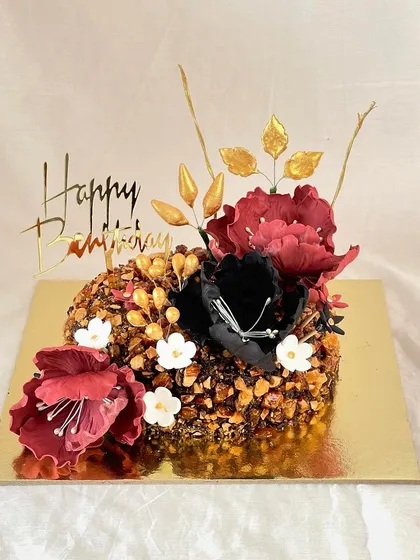 This almond praline cake is decorated with bold, artistic sugar flowers in deep red and black, contrasted with small white blossoms and golden leaves for a dramatic effect.