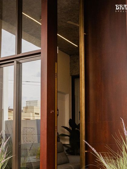The door opens to reveal the connection between the exterior and interior spaces. The continuous line of the 10-foot brass handle acts as a visual anchor, seamlessly bridging the outdoor approach with the welcoming ambiance inside.