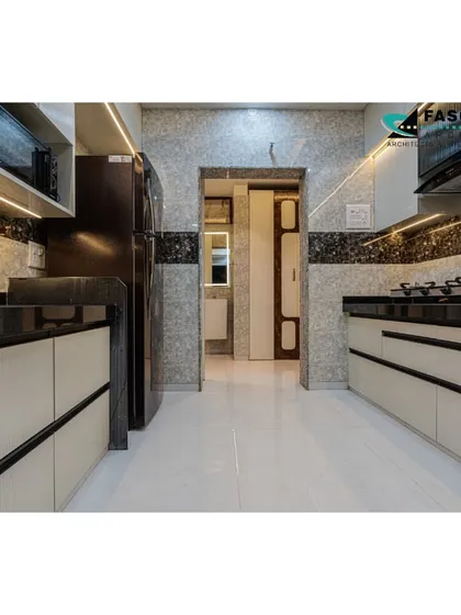 A parallel kitchen layout in Bhiwandi, designed for efficiency. The space features off-white cabinets with black profile handles, a dark granite countertop, and textured wall tiles for a modern, high-contrast look.