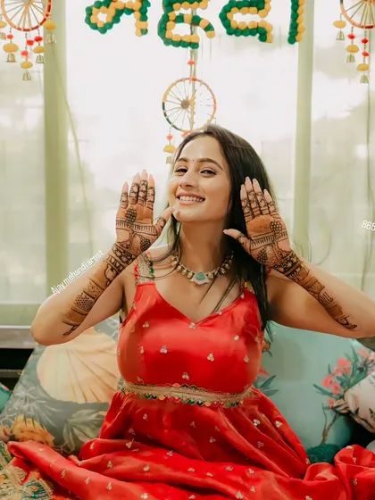 A happy bride showing off her mehndi in front of a festive "Mehndi" backdrop. Her smile says it all.