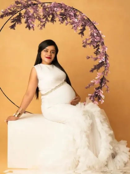 A serene portrait in our white mermaid gown with a ruffled train, seated against a floral hoop for a modern and elegant look.