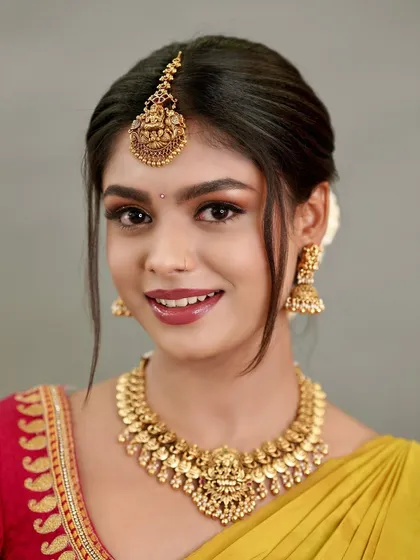 A simple, elegant look can be just as impactful. This client is radiant in a classic Kasina Sara necklace with matching jhumkas and a Laxmi maang tikka, perfect for a pre-wedding pooja or a family function.