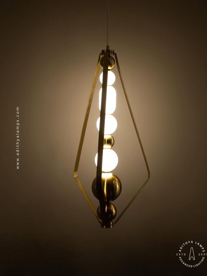 This elegant pendant is framed by a triangular gold structure, enclosing a string of white and gold beads. It's a sophisticated and modern piece that adds a touch of jewelry-like decoration to your space.