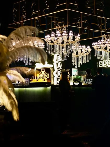 A moody and atmospheric shot of the chandelier-laden bar, with a large feather arrangement adding a touch of old-world glamour. This decor is perfect for a Gatsby-themed soirée.