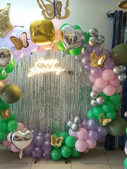 A circular balloon arch with a crown and butterfly theme in green, pink, and purple.