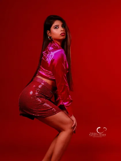 A bold, confident pose that owns the frame. The combination of the red background and sequined outfit creates a high-energy, fashion-forward statement.
