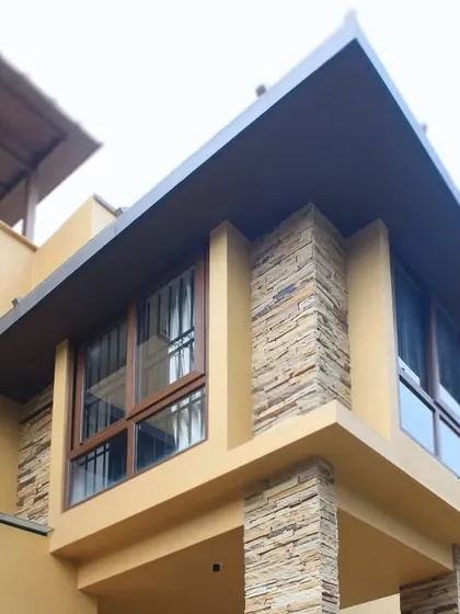 This detailed shot focuses on a corner of the house, showing the precise integration of the stacked stone pillar, large windows, and the angular metal roof.