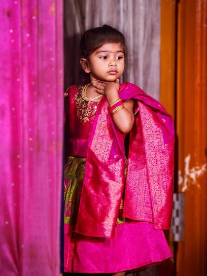 A candid portrait of a little girl in a vibrant pink traditional outfit. The way she's looking off to the side gives the photo a natural and thoughtful quality.