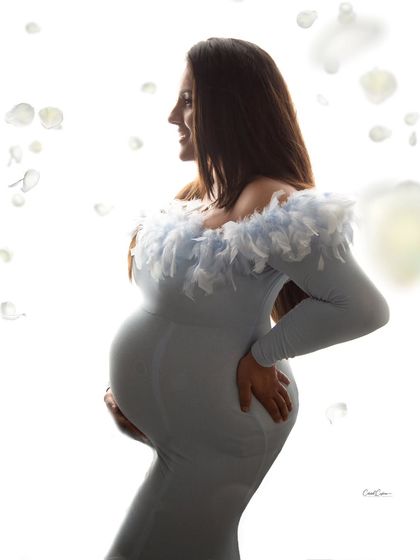 A dreamy, high-key silhouette shot. The mom-to-be is surrounded by floating white petals, creating a soft and angelic feel.