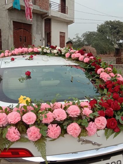 A rear view of a car decorated with pink carnations and red roses. The floral arrangement cascades down the back, ensuring the car looks beautiful from every angle.