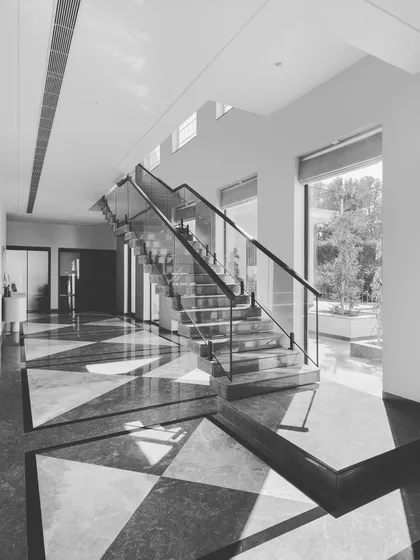 A black and white shot of the sun-drenched hallway and staircase, emphasizing the stunning geometric patterns of the marble floor and the clean lines of the architecture.