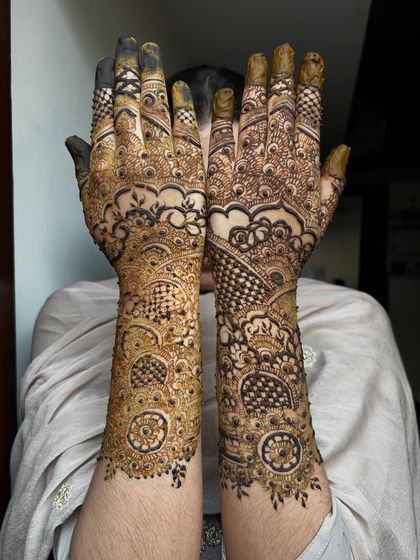 This is a classic Pakistani-style bridal design, characterized by bold outlines and very fine, intricate filler work. The contrast creates a dramatic and elegant effect, covering the arms completely.