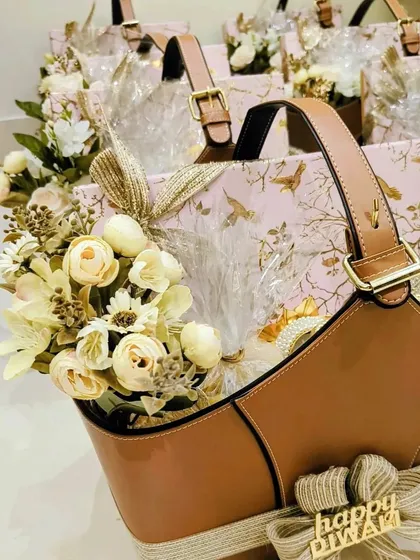A close-up of the Diwali hamper for Red Chillies Entertainment, highlighting the floral arrangement and the "Happy Diwali" tag. The combination of tan leather, pink, and cream flowers creates a sophisticated look.