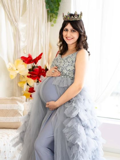 A full-length portrait showcasing a beautiful silver and blue gown. The expecting mother stands confidently, highlighting the intricate details of the dress and her radiant smile.