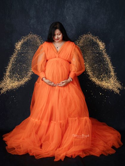 Glowing with magic. This mom-to-be looks absolutely angelic in a flowing orange gown, complete with sparkling wings for a touch of fantasy.