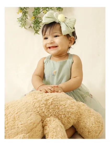 A close-up portrait of a happy baby with her teddy bear. The soft lighting and simple background keep the focus on her adorable smile.