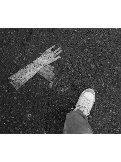 A first-person perspective in black and white, looking down at a discarded mannequin hand on the asphalt of Sarojini Market. It's a strange and surreal detail found amidst the chaos.