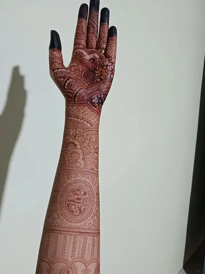 A full arm view of a bridal henna design, showcasing the journey from fingertips to elbow. The pattern includes mandalas, paisleys, and traditional bands, creating a cohesive and stunning piece of art.