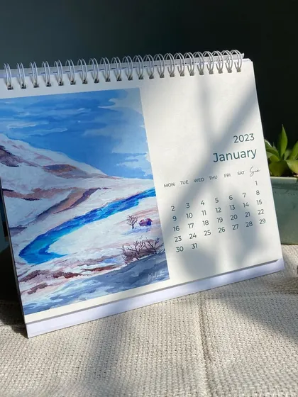 A glimpse of the January page from my 2023 desk calendar. It features a watercolor painting of a snowy landscape with a bright blue river, setting a peaceful and hopeful tone for the start of the year.