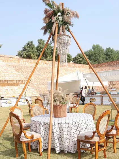 A bohemian-style dining setup with a teepee-like structure, a macrame chandelier, and rustic-chic table settings.