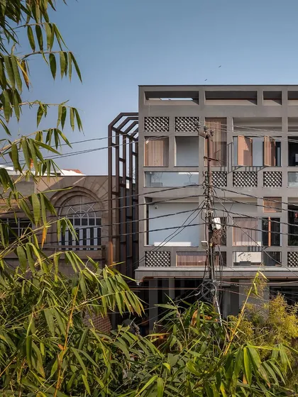 The home's exterior, seen through bamboo leaves, showcases its rugged, industrial aesthetic. The fly-ash bricks and dark raw concrete give the facade its distinctive, resilient character.
