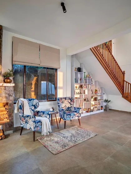 A cozy reading nook by the stone-clad fireplace, furnished with floral armchairs, perfect for enjoying a quiet evening.