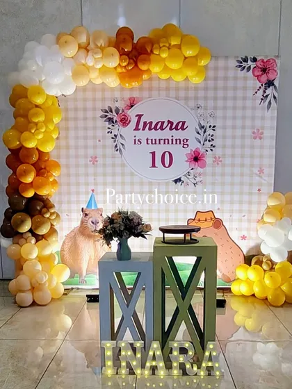 The main backdrop for the Capybara party, with a custom printed gingham background, character cutouts, and a balloon garland in warm, earthy tones.