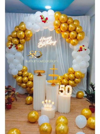 A classic 50th birthday decoration with a circular balloon arch in white and gold. The setup includes a neon sign, marquee numbers, and multiple pedestals for cake and desserts.