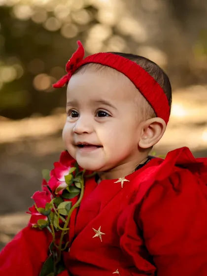 A beautiful close-up of a baby girl in a red dress during her outdoor birthday session. The natural light and her happy smile are just perfect.